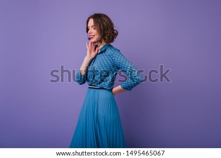 Romantic female model with inspired face expression posing on purple background. Photo of jocund short-haired woman wears elegant long skirt.