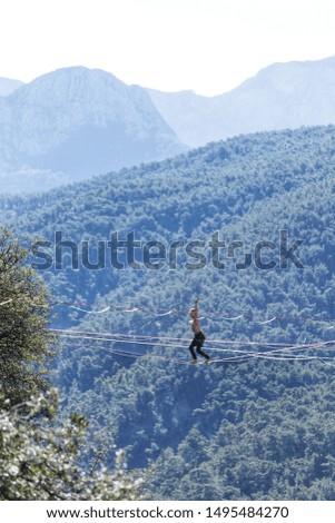 A man is walking along a stretched sling. Highline in the mountains. Man catches balance. Performance of a tightrope walker in nature. Highliner on the background of valley.