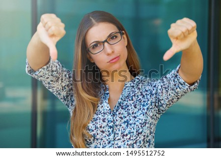 Upset young business woman with thumbs down outdoors.