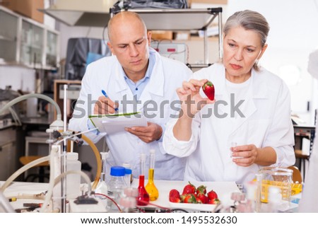 Two experienced biochemists checking fruits and vegetables for nitrates and pesticides in modern laboratory, recording experimental procedure and results

