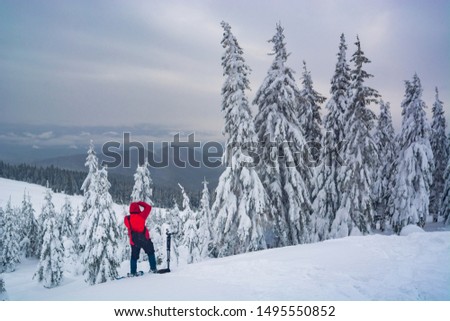 Photographer with a photocamera standing on a hill and take a picture of snowy winter valley.