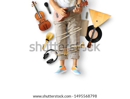 Young man sits and plays guitar among musical instruments