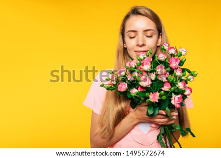 Beautiful smell. Portrait of lovely blonde woman while she is trying the smells of roses in her hands. Holidays and gifts concept. Women's day. St. Valentine's day