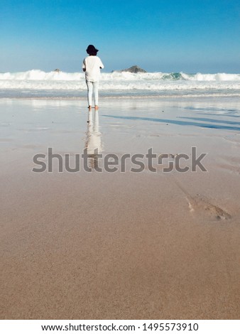 a woman stood looking at the beach with small waves in the afternoon