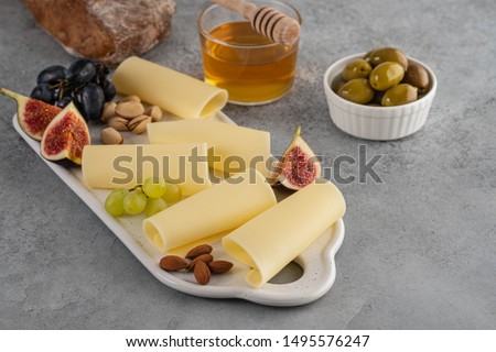 Cheese slices on white board with honey, figs, olives, grapes.