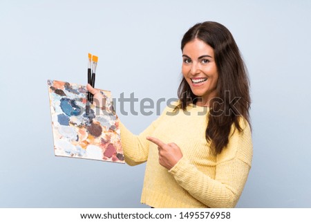 Young artist woman over isolated blue background and pointing it