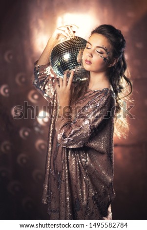 Beautiful girl holding a disco ball in her hands from pieces of a mirror, studio portrait, brown background