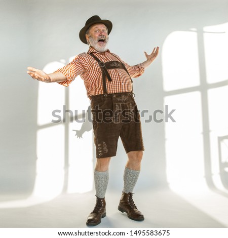 Portrait of Oktoberfest senior man in hat, wearing the traditional Bavarian clothes. Male full-length shot at studio on white background. The celebration, holidays, festival concept. Happy calling.