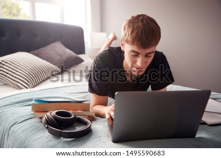 Male College Student Lies On Bed In Shared House Working On Laptop Royalty-Free Stock Photo #1495590683