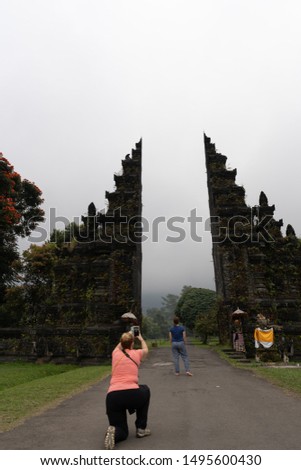 A tourist taking picture of her friend using smartphone on Handara Gate, Bali