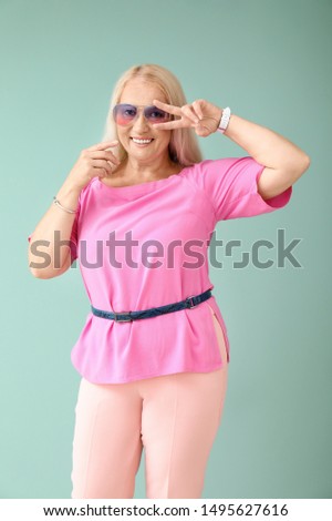 Stylish mature woman showing victory gesture on color background