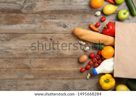 Flat lay composition with overturned paper bag and groceries on wooden table. Space for text
