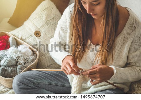 Beautiful girl knits a warm sweater on the bed. Knitting as a hobby. Accessories for knitting.