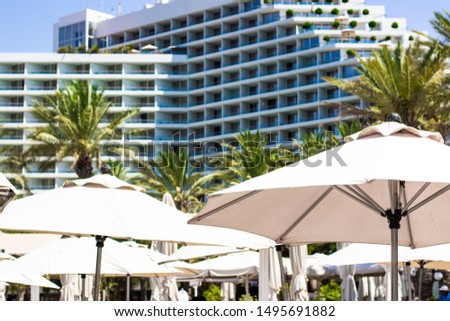 summer vacation destination hotel apartment huge building front yard with palm trees and white umbrellas in season sunny weather time 