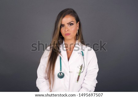 Portrait of outraged young doctor woman with oval face, frowning her eyebrows being displeased with something. Scowling pretty female isolated over grey.
