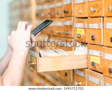 Student making photo cards in old wooden card catalogue using smartphone