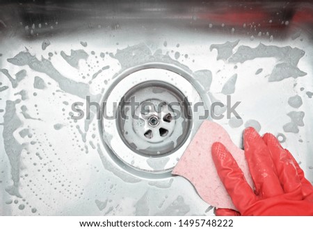 Closeup sink drain and hand wearing organge rubber glove cleaning scrub steel sink with sponge. Housework concept