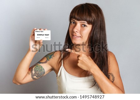 Finance and Bank cards. A young woman with tattoos smiling and holds a Bank card and points at it with her finger