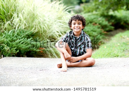 Full Body picture of Beautiful Biracial African American Black Boy Happily sitting outdoor at nature park in the summer