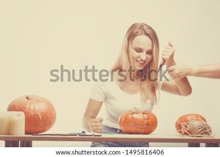 Halloween concept, happy Girl sitting at table with pumpkins preparing for holiday with candle and rope, cut Jack lantern, funny and spooky pumpkin. Trick or treat tradition. Hand stop knife
