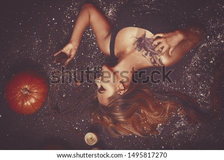 Halloween concept, girl vampire with red eyes red lips lying on floor with pumpkins and snow around. Scary crazy woman trick or treat time. Female makeup for holiday with candle