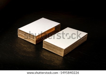 A mockup for two stacks of white business cards with golden painted edges on a black background with copy space