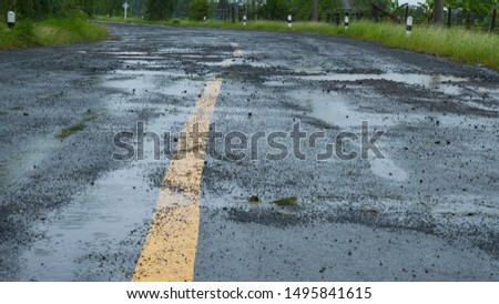 Pothole and Cracked asphalt road with yellow dividing line