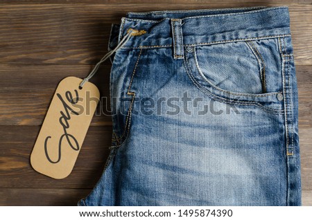 Denim. Blue jeans on brown wooden background. Sale - handwritten inscription on a paper label.