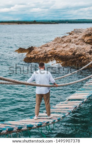 man walking by suspension bridge cross sea bay rocky cliff summer time