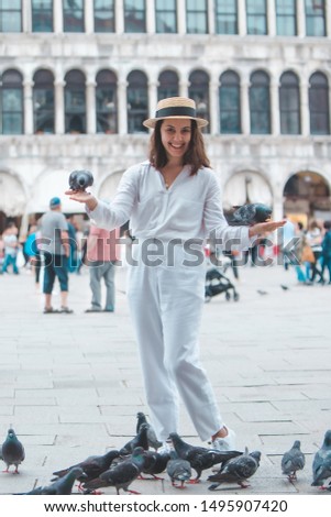 woman in white clothes with straw hat having fun with pigeons at venice city square piazza san marco