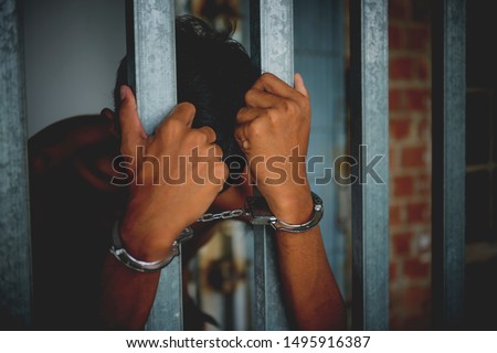 The man in the handcuffs is behind the bar in the police station. He was imprisoned. He took off his shirt.
 prisoner concept - picture Royalty-Free Stock Photo #1495916387