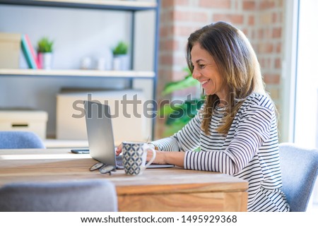 Middle age senior woman sitting at the table at home working using computer laptop with a happy face standing and smiling with a confident smile showing teeth