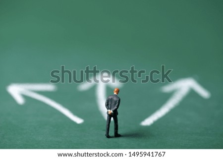 miniature people stand on green chalk board and select direction