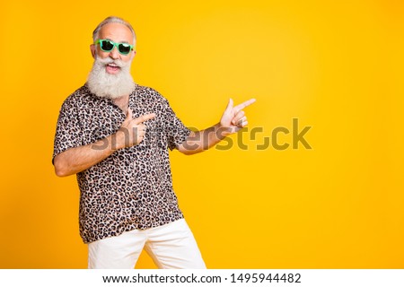 Portrait of crazy funny funky old bearded man with eyeglasses eyewear point at copyspace recommend sales discounts  wear leopard print shirt isolated over yellow  background