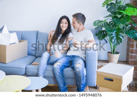 Young beautiful couple sitting on the sofa drinking coffee at new home around cardboard boxes