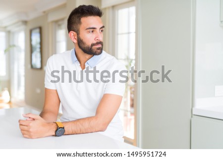 Handsome hispanic man casual white t-shirt at home looking to side, relax profile pose with natural face with confident smile.