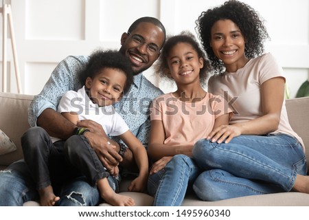 African married couple and little adorable children embracing sitting together on couch in living room at home looking at camera photographed for memory, happy mixed-race full family portrait concept Royalty-Free Stock Photo #1495960340