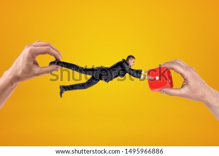 Big male hand holding tiny businessman who is reaching to another big hand holding red casino dice on yellow background. People and objects. Digital art. Risk and reward.