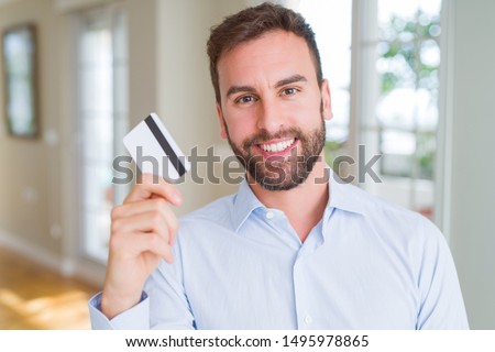Handsome business man holding credit card with a happy face standing and smiling with a confident smile showing teeth