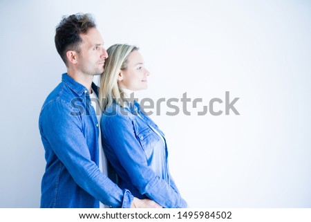 Young beautiful couple wearing denim shirt standing over isolated white background looking to side, relax profile pose with natural face with confident smile.