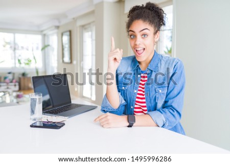 Young african american business woman working using computer laptop pointing finger up with successful idea. Exited and happy. Number one.