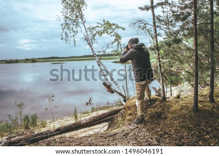 A man in a gray jacket, take a photo of nature on the banks of the river, in the fores