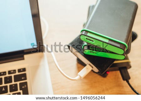Many external hard drives on wooden table next to laptop computer, busy working photographer