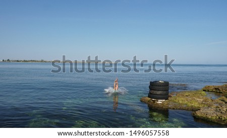 Skilled diver jumping to the deep blue sea. Beautiful sea and blue sky with old tires on the coast.