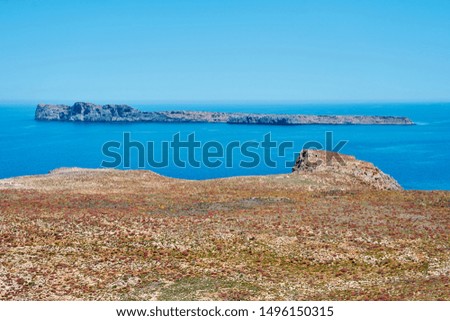                     Rocky sea shore with blue sea and island on a horizon on a background in Crete, Greece.           