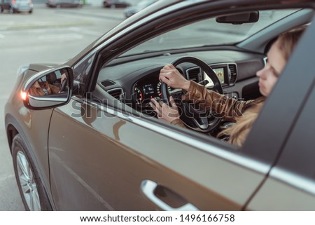 A girl driving a car, looks in a side view mirror, parking at shopping center, turning at an intersection, turning on a turn signal on a car. Left turn. Woman in a leather jacket. Royalty-Free Stock Photo #1496166758