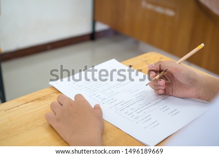 English exams test student in school, university students holding pencil for testing exam writing answer sheet or exercise for taking in assessment paper on table classroom. Education study Concept Royalty-Free Stock Photo #1496189669
