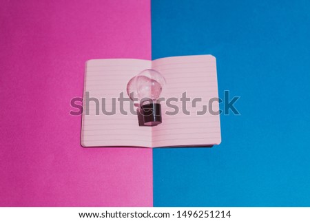 open notebook with blank pink pages and lightbulb above it on contrasting magenta and blue background