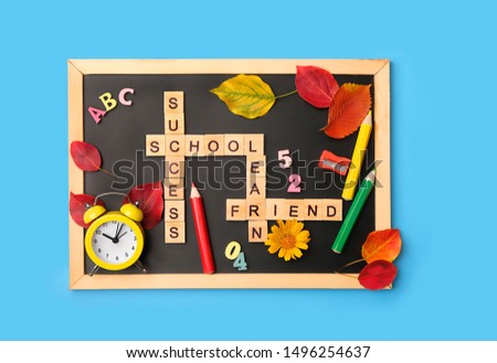 back to school background. crossword wooden letters, supplies, alarm clock, autumn leaves and black chalkboard on blue backdrop. beginning of school year, education. flat lay. template for design