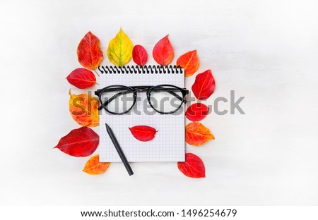 fall season. Autumn bright leaves, eyeglasses, pen, notepad on white background. Creative shape leaves in women face. Minimal art design. copy space